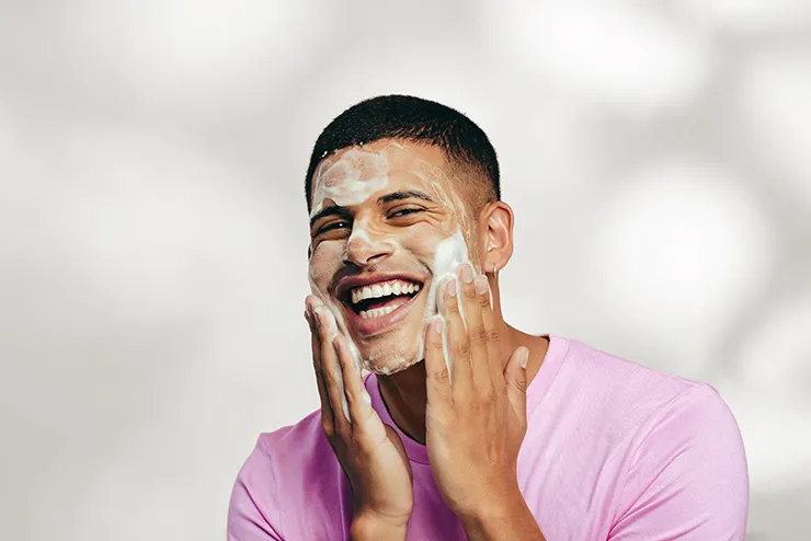 Mann reinigt sein Gesicht mit Schaum und lächelt (Pflegeroutine).