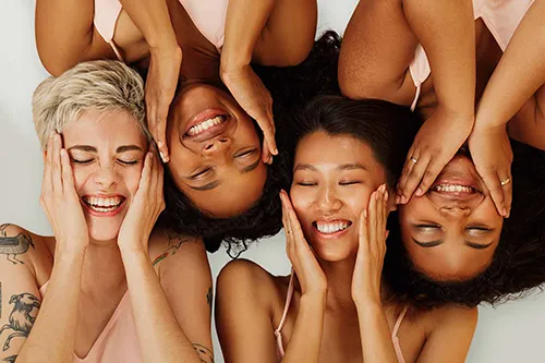 Vier Frauen unterschiedlicher Hauttypen lächeln und halten die Hände an ihr Gesicht (Hautwissen).